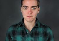 Headshot of a person wearing a plaid green and black shirt looking into the camera