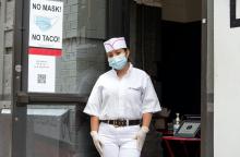 Worker at taco restaurant in front of sign that reads "no mask no taco"