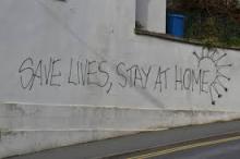 Graffiti on a wall saying, "Save Lives, Stay Home"