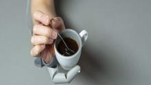 Hand with extra robotic thumb stirring coffee with a spoon