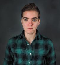 Headshot of a person wearing a plaid green and black shirt looking into the camera
