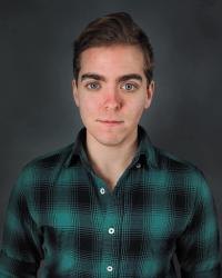 Headshot of a person wearing a plaid green and black shirt looking into the camera