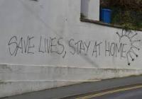 Graffiti on a wall saying, "Save Lives, Stay Home"